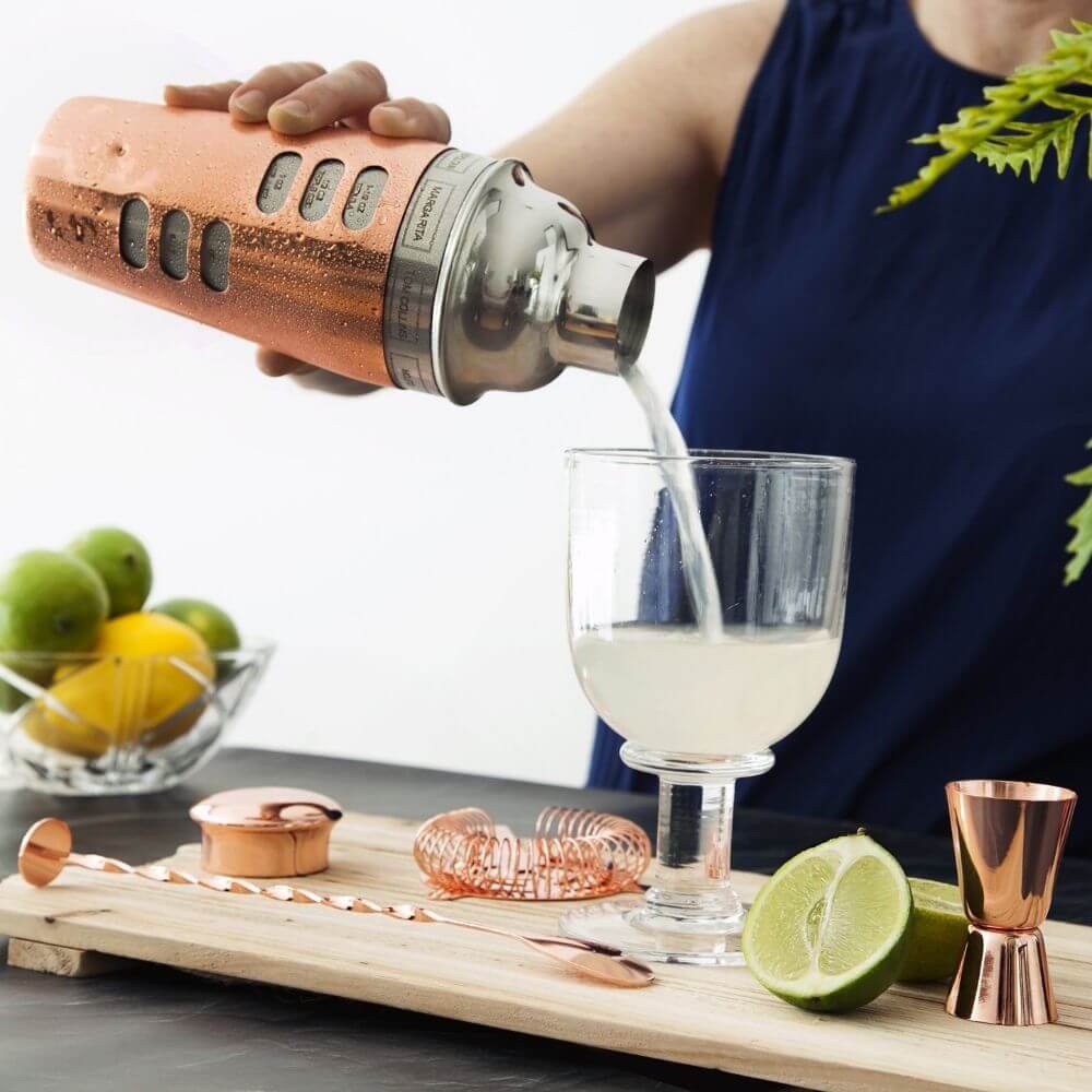 A cocktail being poured into a glass from a shaker
