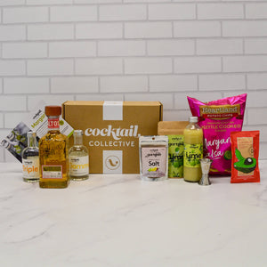 Margarita Night Kit on a bench top with Altos tequila, Triple Sec, citrus chilli salt, lime wheel garnish, lime juice, spirit measure, margarita chips and salsa, and gourmet spicy guacamole dip