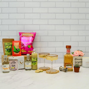 Margarita Night Kit on a bench top with Altos tequila, Triple Sec, citrus chilli salt, lime wheel garnish, lime juice, spirit measure, margarita chips and salsa, gourmet spicy guacamole dip and two margaritas in ribbed cocktail coupes with a salted rim