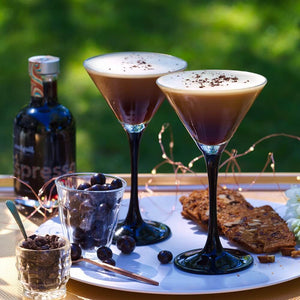 Two Espresso Martini cocktails sitting on a tray with a glass of coated coffee beans & a bottle of Espresso Liqueur from Cocktail Collective