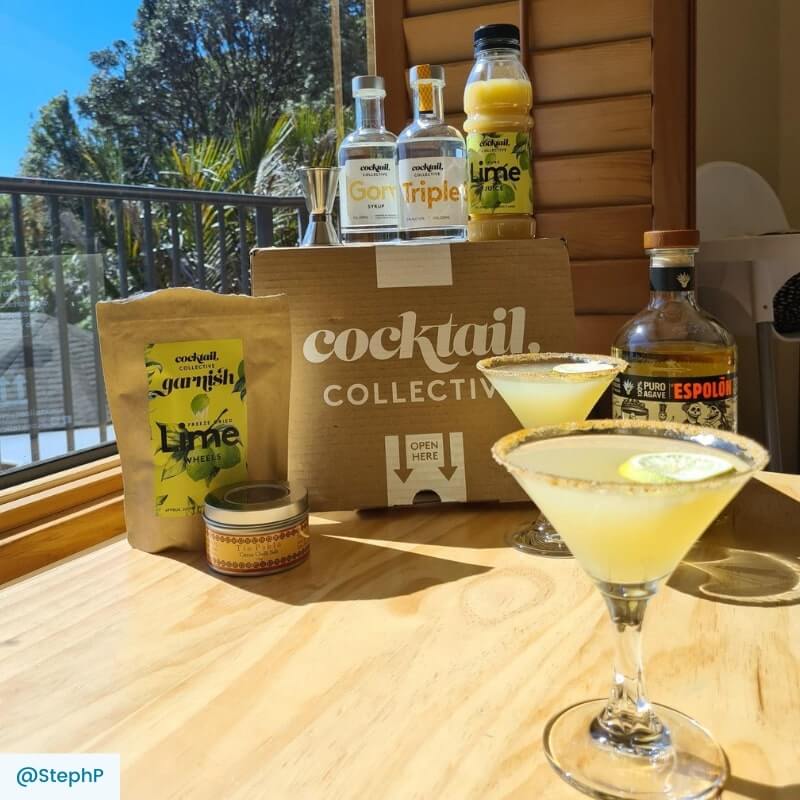 The Margarita cocktail box with ingredients and 2 cocktails in martini glasses 
