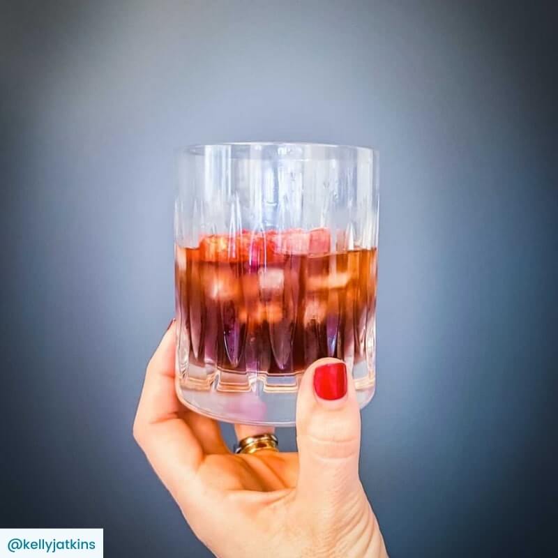 Negroni cocktail in a crystal tumbler held in woman's hand with grey backgound