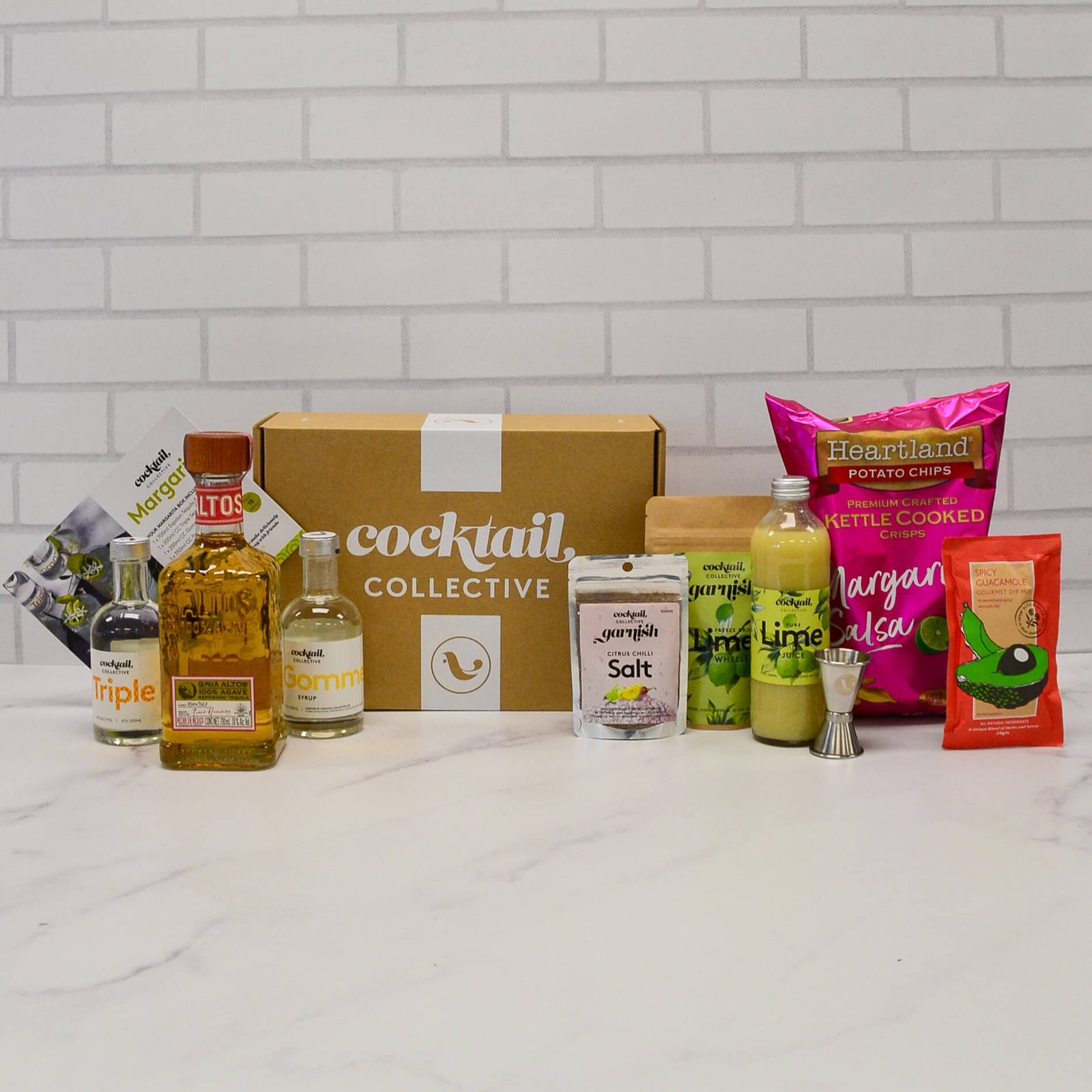 Margarita Night Kit on a bench top with Altos tequila, Triple Sec, citrus chilli salt, lime wheel garnish, lime juice, spirit measure, margarita chips and salsa, and gourmet spicy guacamole dip 