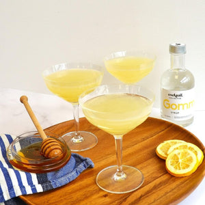 Three Bee's knees cocktails with honey, lemon wheels and honey dipper