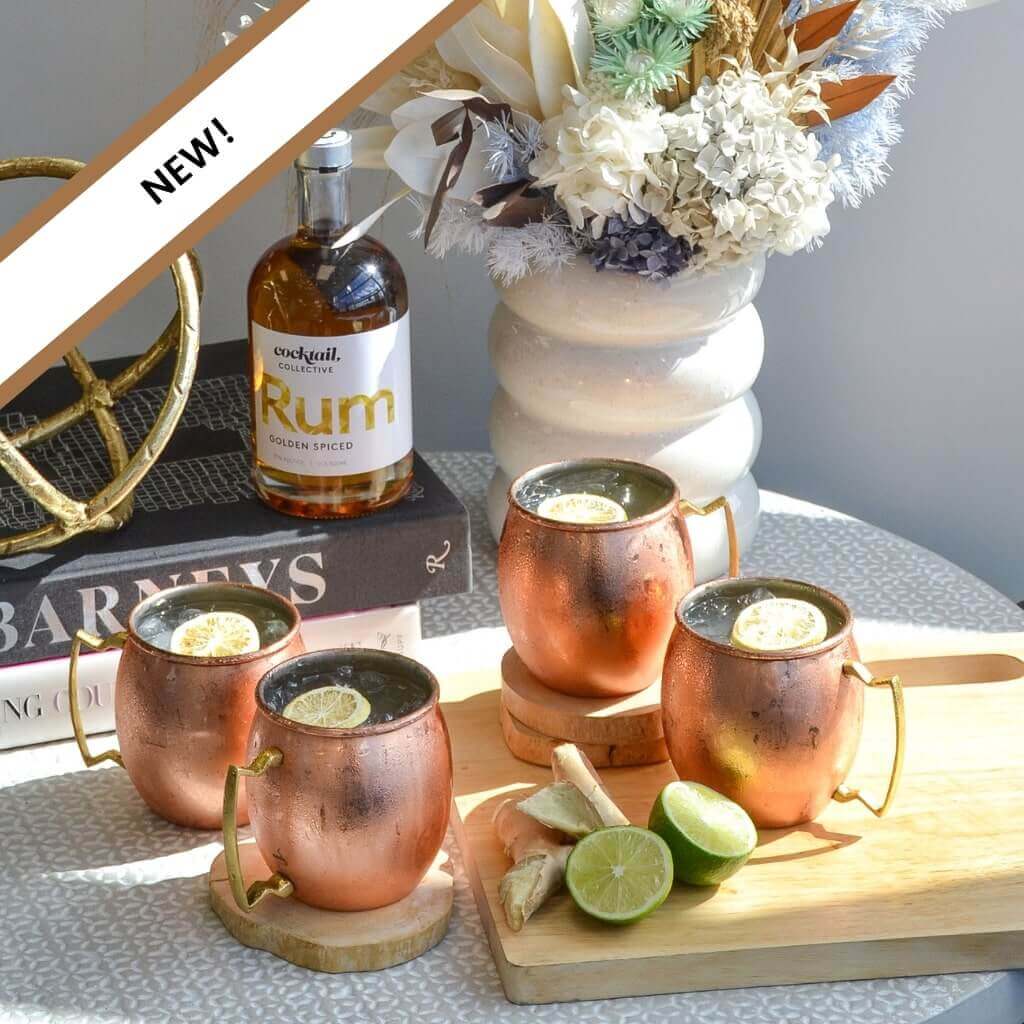 Four Spiced Rum Moscow Mule Cocktails in copper mugs on a table with ginger and lime