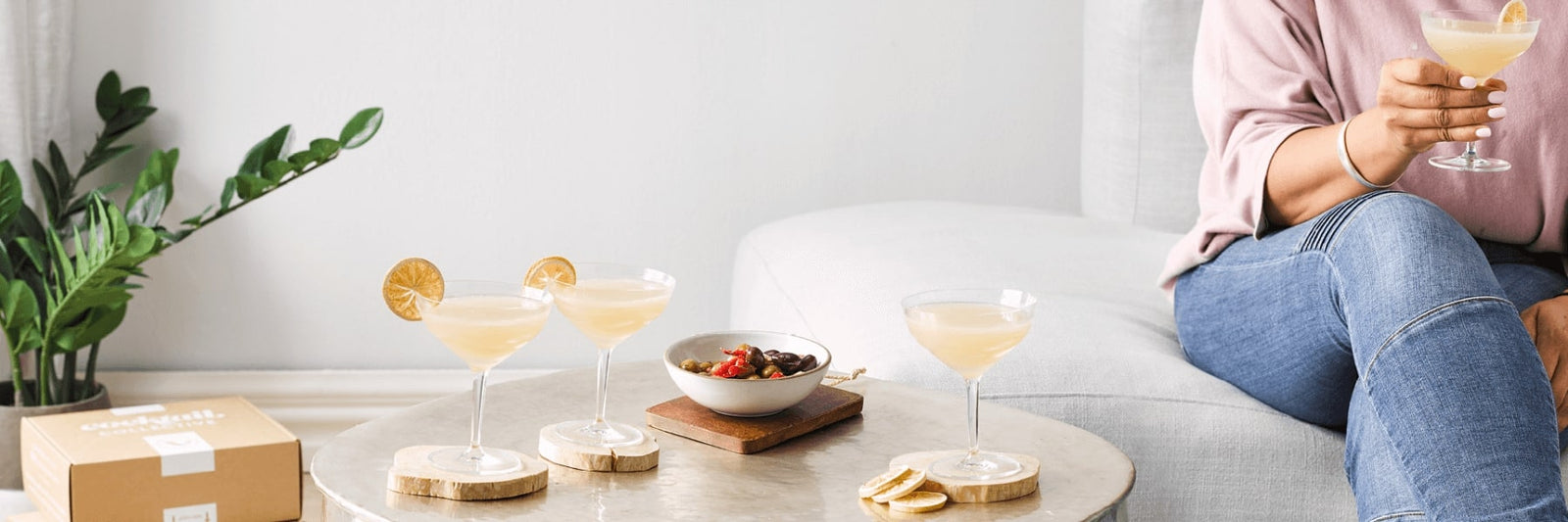 Cocktail Collectives gift boxes on the floor next to a table with three cocktails