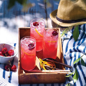 3 ruby red coloured Beachcomber cocktails, garnished with cherries in tall highball glasses, sitting on a tray outside in the dappled summer sunlight | Cocktail Collective