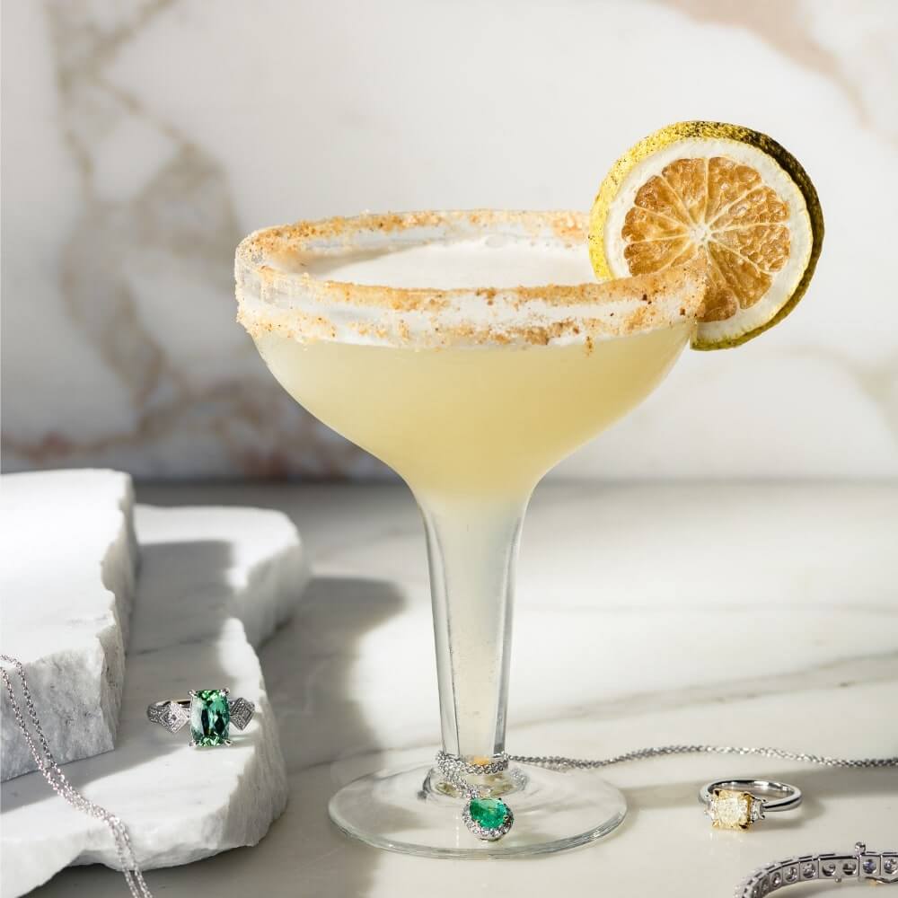 Deluxe Margarita Cocktail in coupe glass with lime wheel garnish, displayed on a bench with jewellry beside it