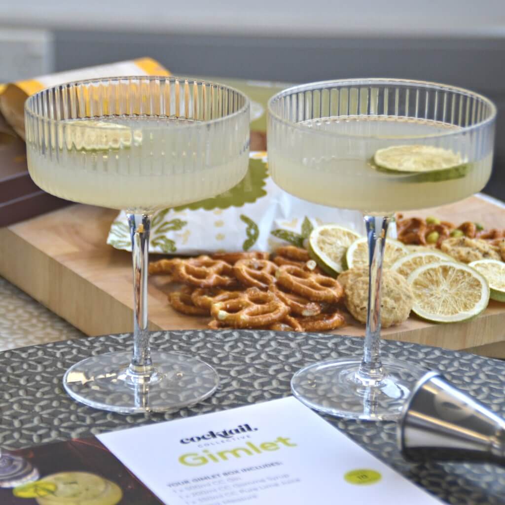 Two Gin Gimlet cocktails in coupes with assortment of snacks