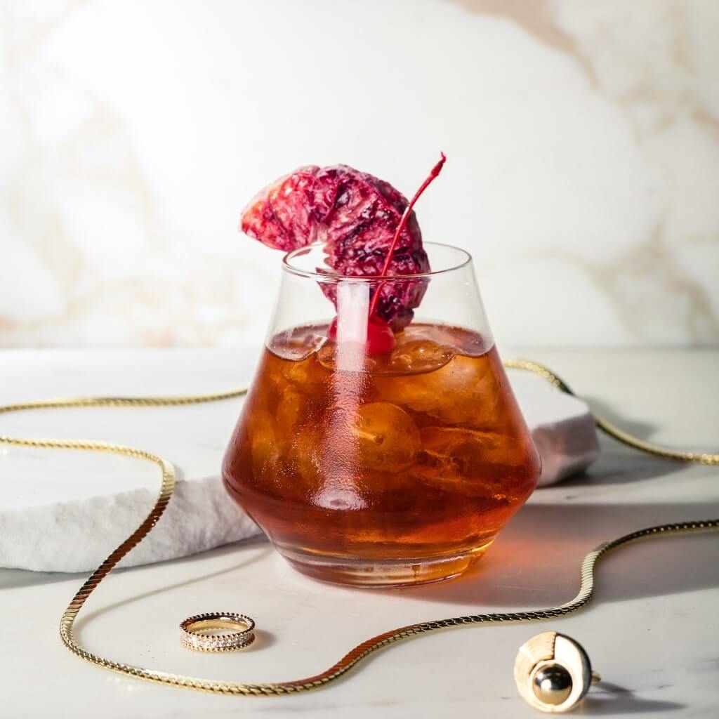 Cocktail Collective's Spiced Rum Old Fashioned garnished with a cocktail cherry and blood orange cocktail garnish.