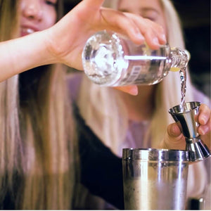 2 girls mixing cocktails. Pouring Gomme Syrup into a spirit measure.
