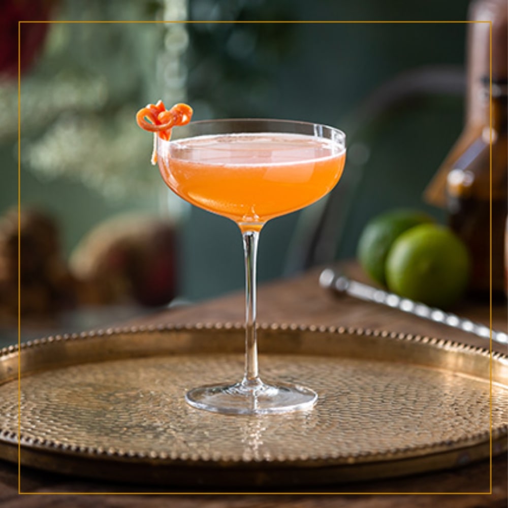 A Toreador cocktail garnished with an apricot twirl served on a copper tray.